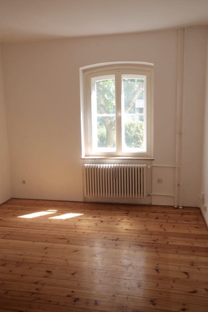 Spacious empty room with wooden floor and large window in Berlin, ideal for interior planning.